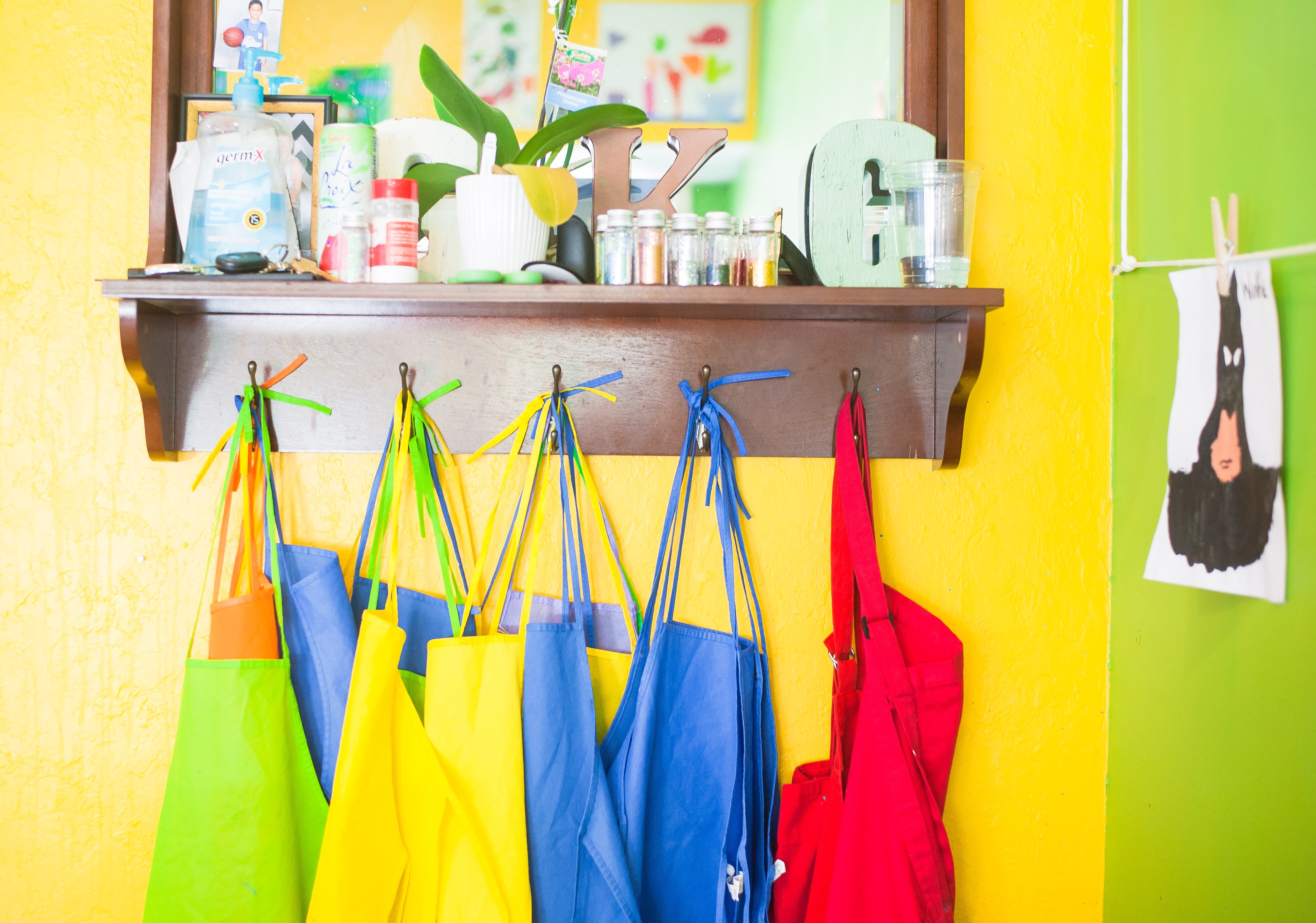Brightly coloured aprons hang on yellow classroom wall